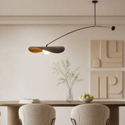 Modern black and wood pendant light above a dining table with minimalist wall art.