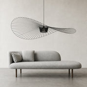 Gray rounded chaise sofa with two pillows beneath a sculptural black wire pendant light.