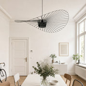 Black wire pendant light shaped like a sweeping leaf in a bright minimalist room.