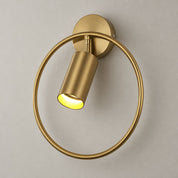 Brass circular wall sconce with a tilted lit cylinder shade on a plain wall.