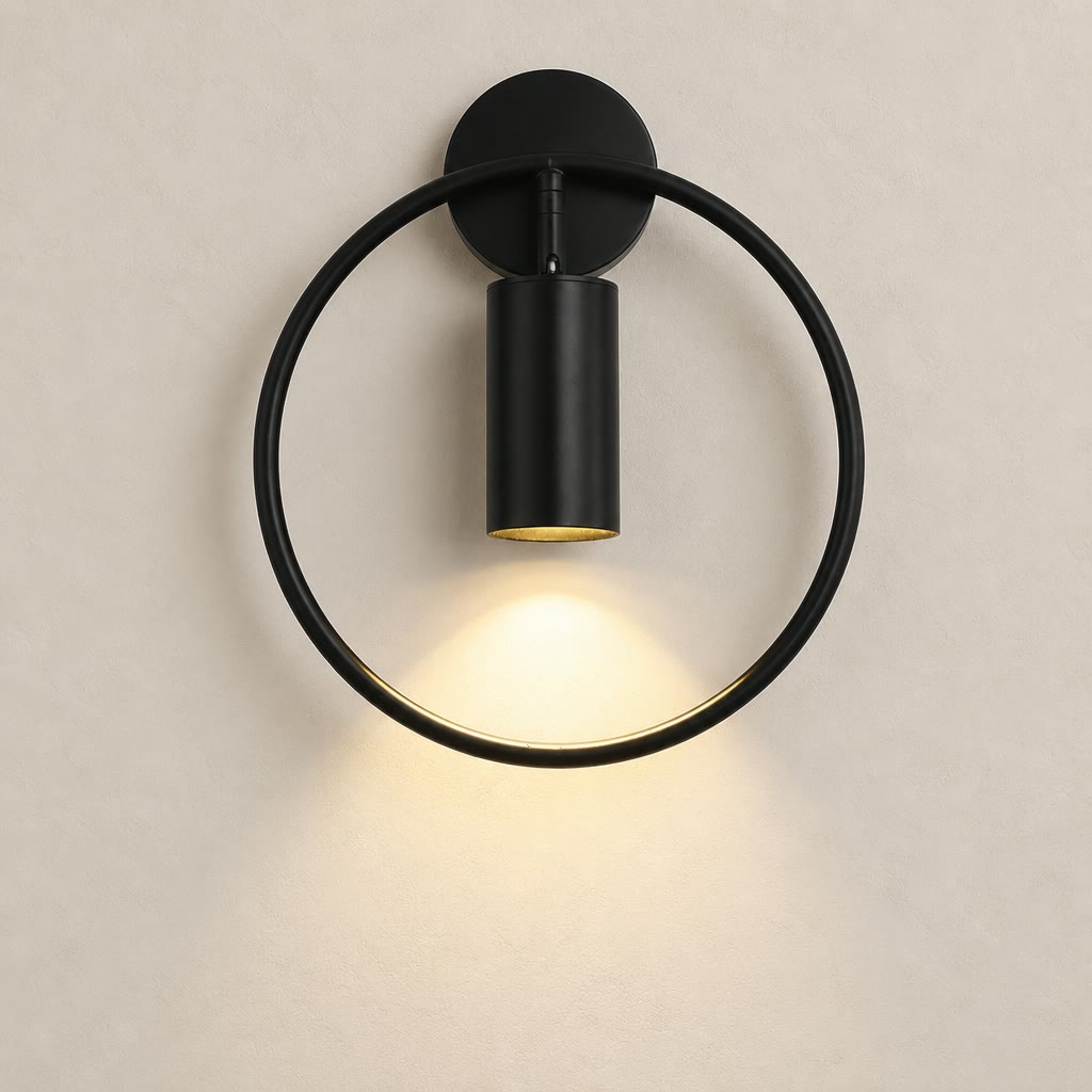 Black circular wall sconce with a cylindrical downlight casting a warm glow on a pale wall.
