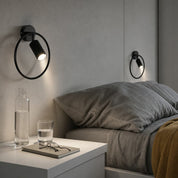 Black circular wall-mounted reading lamps illuminate a modern bedside scene.