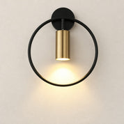 Black and brass circular wall sconce casting warm light on a pale wall.