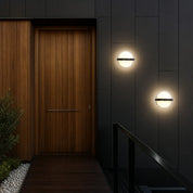 Modern circular wall lights on dark exterior panels beside a warm wooden entry door.