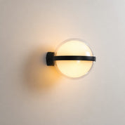 Black wall sconce with a glowing round frosted globe on a pale wall.