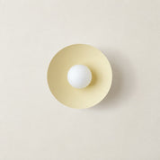 Cream circular wall sconce with a centered white globe bulb on a neutral wall.