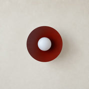 Burgundy circular lamp shade with a central white globe on a warm neutral wall.