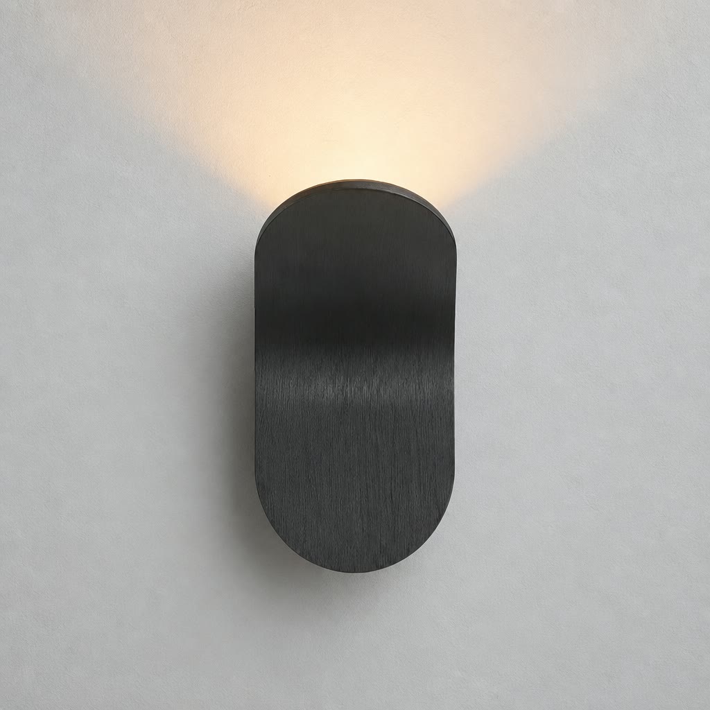 Black rounded wall sconce casting a warm glow on a pale wall.