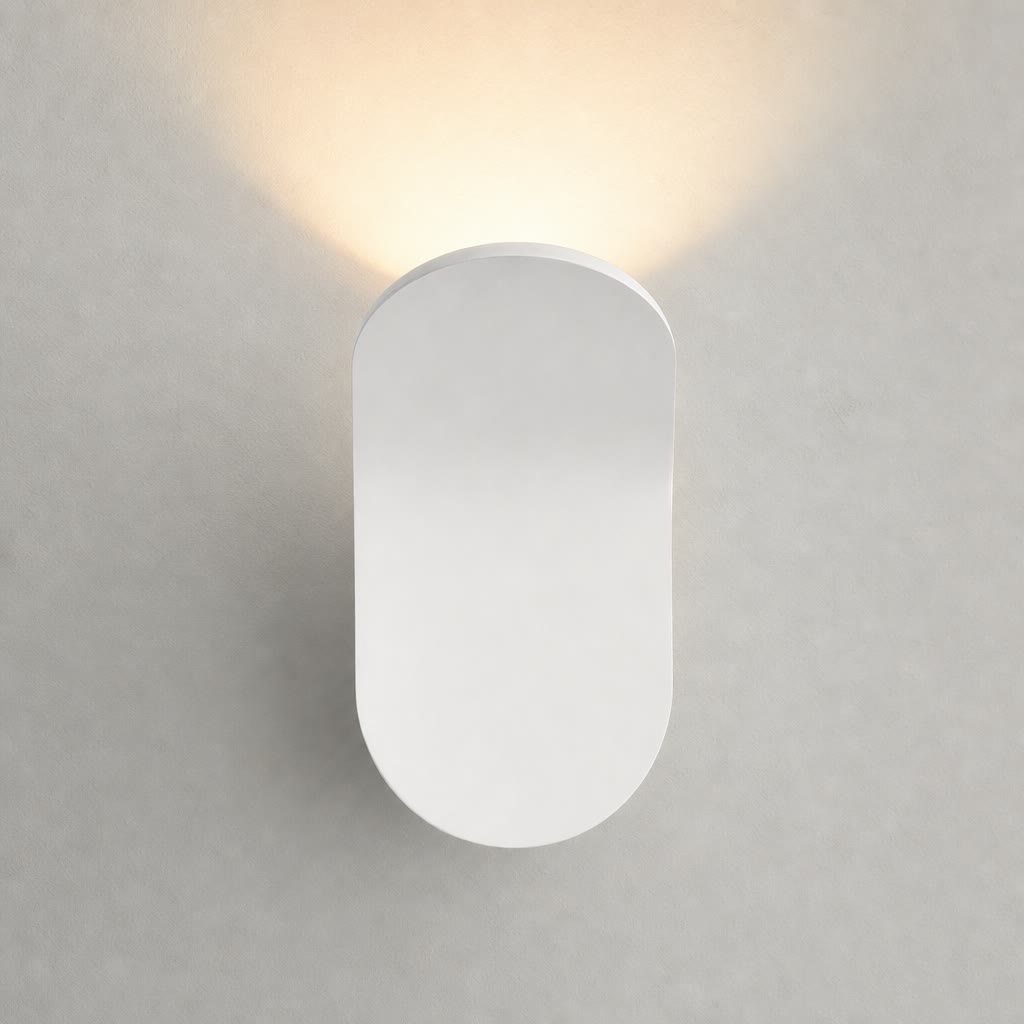 White capsule wall sconce emitting a warm upward glow on a pale wall.