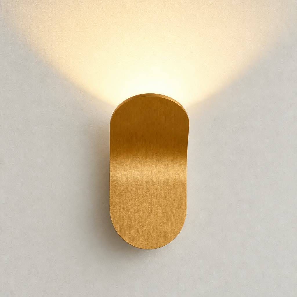 Gold capsule wall sconce with warm upward glow on a pale wall.