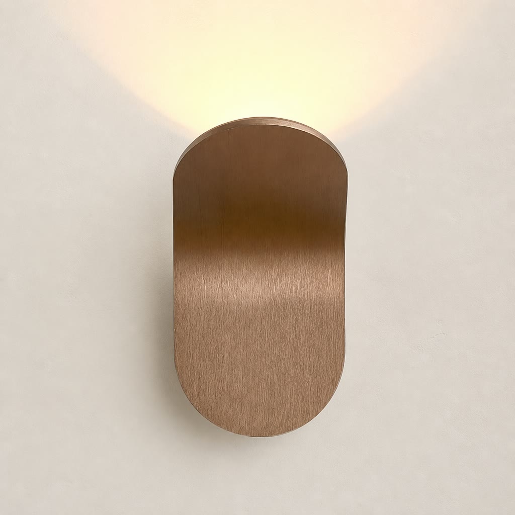 Brushed bronze rounded wall sconce casting a warm glow on a pale wall.