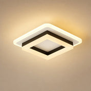Square warm ceiling light with layered white frame and black inner trim glowing on a beige background.