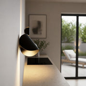Black wall-mounted spotlight with warm glow above a sleek kitchen counter.