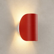 Red half-cylinder wall sconce on a textured pale wall casting a warm glow.