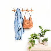 Wooden wall coat rack holding a denim jacket and tan leather shoulder bag.