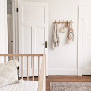 White paneled door beside a wooden peg rail with hanging bags and a rainbow wall charm.