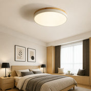 Round wood-trim ceiling light above a warm modern bedroom with bed and window.