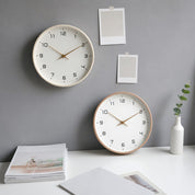 Two minimalist round wall clocks with white faces and gold hands on a gray wall.