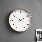 Round wall clock with a wood rim, white face, black numerals, and brown hands on a gray wall.