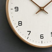 Close-up of a wooden-rim wall clock with a white textured face and black numbers.