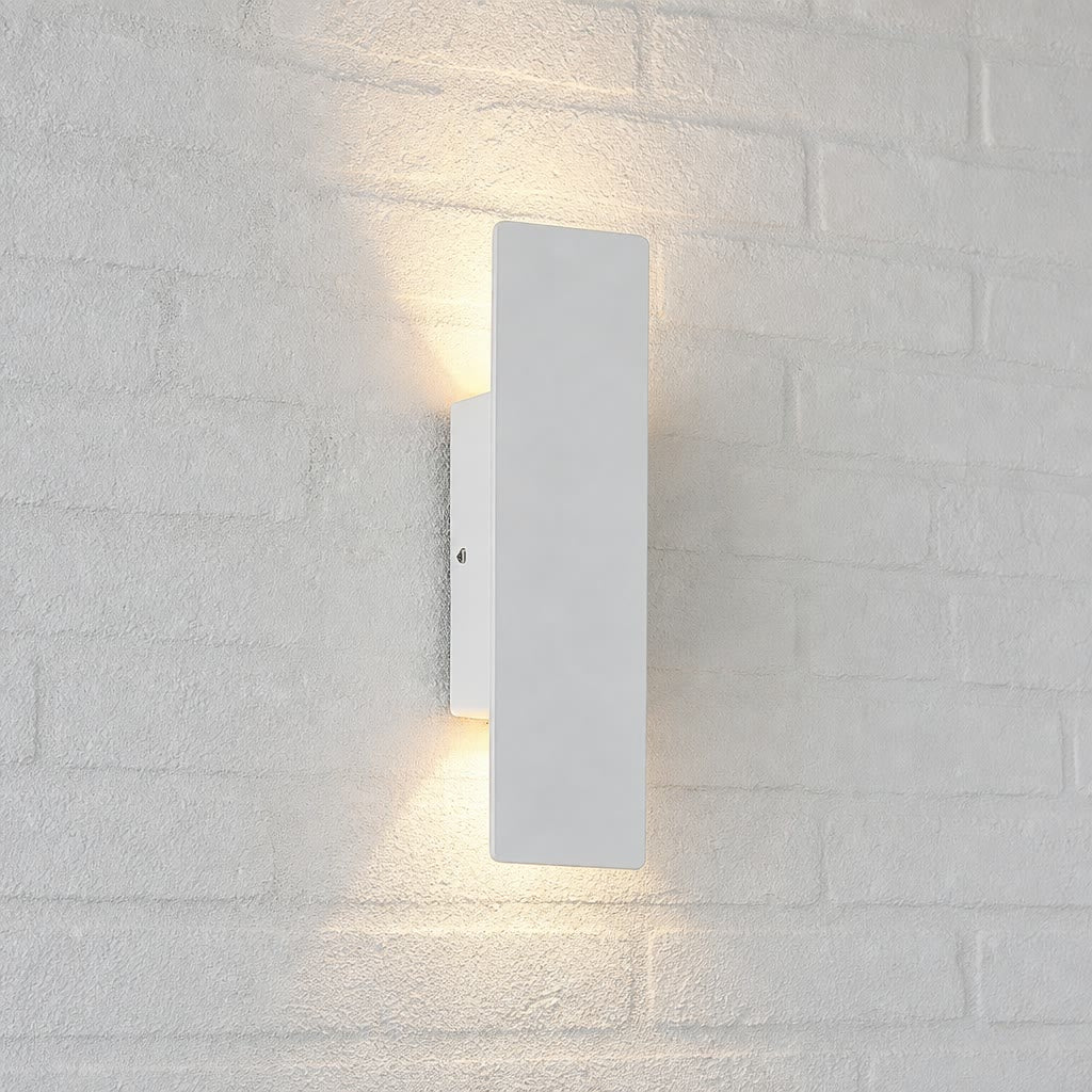 White rectangular wall sconce casting warm up and down light on a white brick wall.