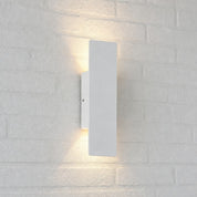 White rectangular wall sconce casting warm up and down light on a white brick wall.