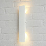 Slim white vertical wall light glowing warmly on a white brick wall.
