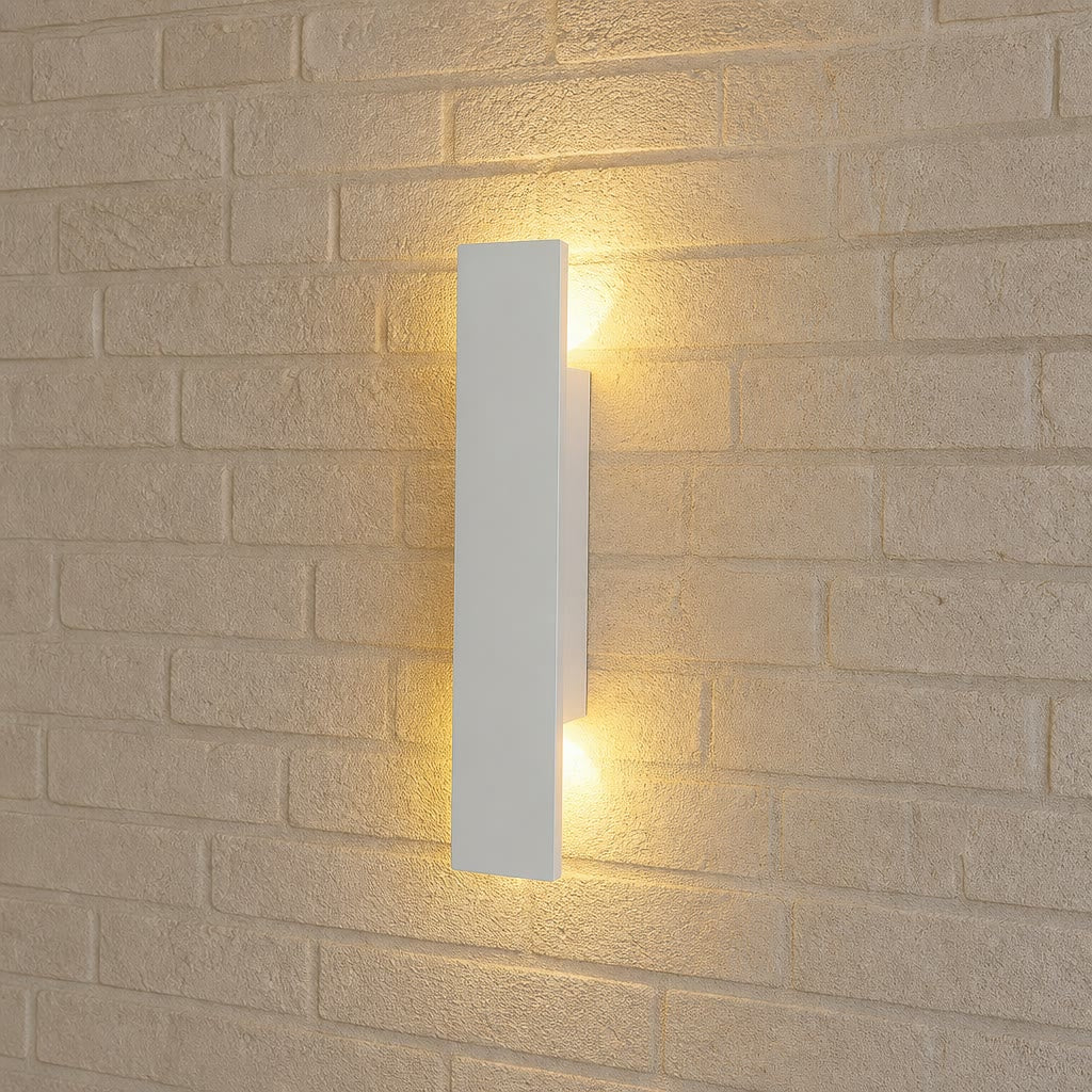 White rectangular wall sconce casting warm light on a beige brick wall.
