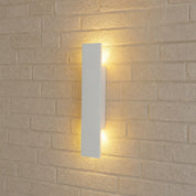 White rectangular wall sconce casting warm light on a beige brick wall.