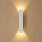 White rectangular wall light casting warm beams on a textured beige wall.