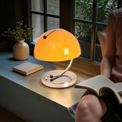 Glowing orange dome table lamp with chrome curved stem on a window bench.