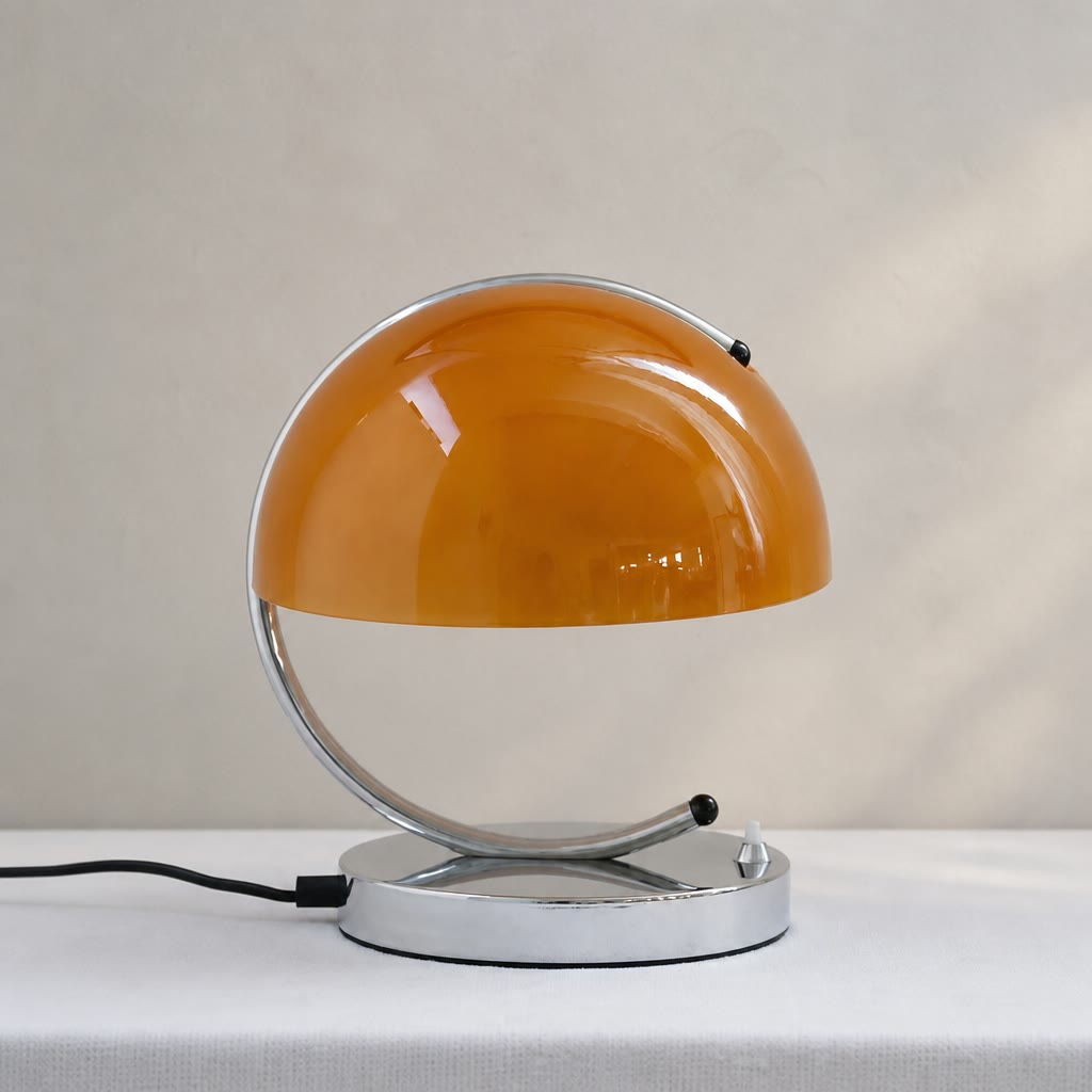 Glossy orange dome table lamp with chrome base and curved metal support on a white surface.
