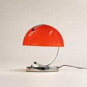 Glossy red dome table lamp with chrome curved stem and base on a neutral background.
