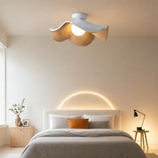 Ceiling lamp with wavy wood shade glowing above a neatly made bed in a warm minimalist bedroom.