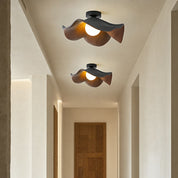 Two sculptural wood and black ceiling lights with glowing bulbs in a warm hallway.