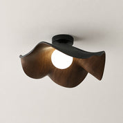 Wavy dark wood ceiling light with a glowing round bulb and black mount.