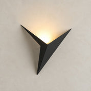 Black angular wall sconce with warm light glowing upward on a pale wall.