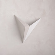 A minimalist, white, v-shaped Starry Night wall sconce against a textured, light-colored wall.