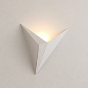 White angular wall sconce glowing warmly on a pale minimalist wall.