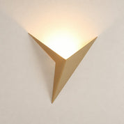 Gold geometric wall sconce casting a warm glow on a plain light wall.