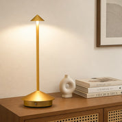 Gold cordless table lamp with round base and slim stem on a wooden console.