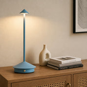 Blue touch table lamp with conical shade and round base glowing on a wooden cabinet.