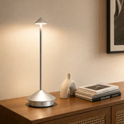 Silver touch table lamp with a slim pole and glowing cone shade on a wooden console.
