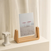 Wooden acrylic photo frame holding a beach umbrella print on a cream shelf.