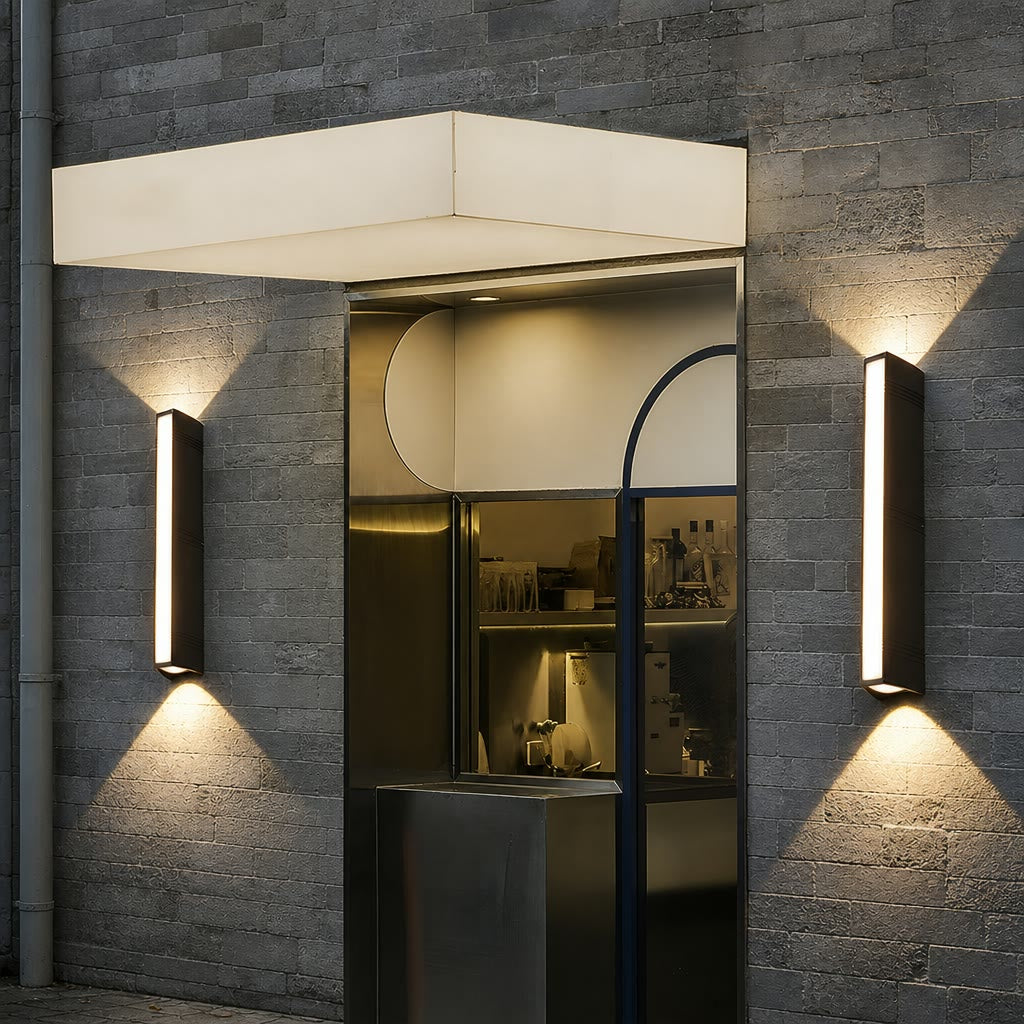 Two slim rectangular wall lights illuminate a gray brick storefront entrance.