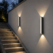 Two black vertical outdoor wall lights glow warmly beside stone stairs.