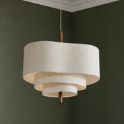 Tiered cream fabric pendant light with warm wood stem hanging in a green room.