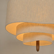 Layered beige fabric ceiling lamp with warm glow and a small wooden finial.