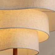 Layered beige fabric lampshade with warm glowing tiers and a wooden center stem.