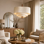 Tiered cream fabric pendant light with a wooden stem hanging in a warm neutral living room.